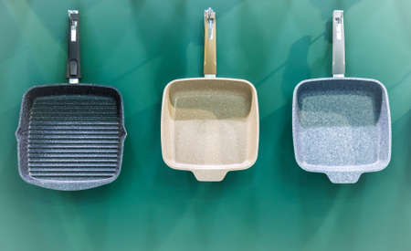 Many aluminum metal new modern cooking pans hang on the wall in the kitchen. Household goods, dishes, kitchen utensils. Storefront, sale of domestic products, interior details, home space organization.の写真素材