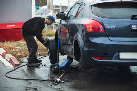 Saratov, Russia - 01/11/2020: Tire service, car service, profession, a male mechanic raises a car with a jack, a serviceman replaces a summer wheel with a winter one.のeditorial素材
