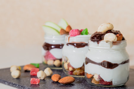 Sweet tasty milk curd creamy food in a glass jar of homemade breakfast. Cheesecake, English Trifle, Eton dessert, tiramisu, zuppa Inglese with nuts, almonds, cashews, hazelnuts, candied fruits and chocolate sauce.の写真素材
