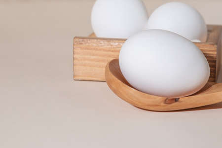 Chicken eggs in a wooden box on beige background with copy space, product with amino acids choline...