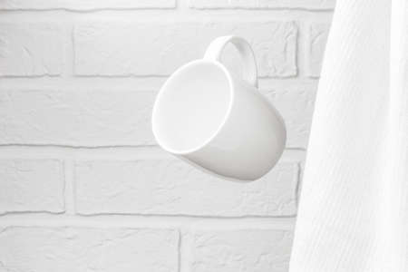 Creative levitation of a white cup against the background of a kitchen stone brick wall and milky-colored textiles, clean tableware concept.の写真素材