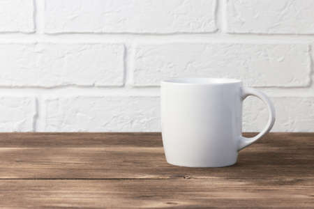 Household utensils, a white cup stands on a shelf on a wooden table against the background of a kitchen stone brick wall of a milky shade, the concept of clean dishes.の写真素材