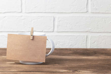 Household utensils, a white cup stands on a shelf on a wooden table against the background of a kitchen stone brick wall of a milky shade, the concept of clean dishes.の写真素材