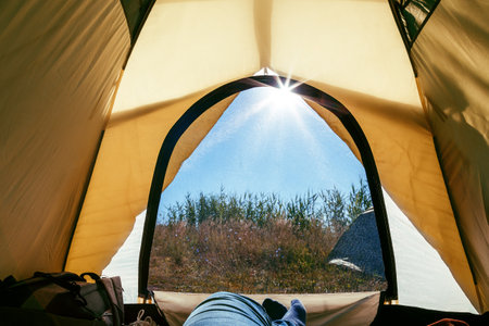 Camping, outdoors, tourism, travel. View from the tent inside on the blue sky sun rays in the summer early morning at sunrise through the mosquito net.の写真素材