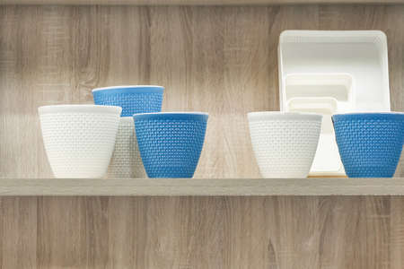 New plastic colorful flower pots white and blue on a shelf against a wooden wall background, household supplies for home and garden decor on a display case.の写真素材