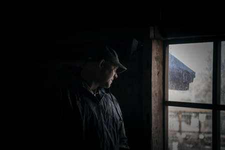 Silhouette of a suspicious strange man looking out the window in a scary dark attic of an old...