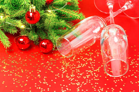 Christmas New Year greeting holiday card with wine glasses, fir tree, golden sparkles, glowing garland on red background.の写真素材
