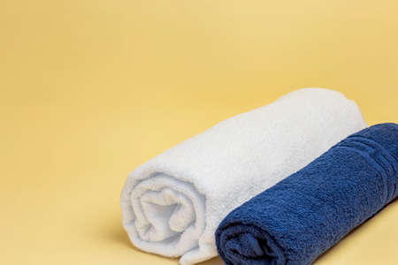 Textile industry, household goods. New cotton terry towel rolled into a roll white and blue on a yellow background with copy space.の写真素材