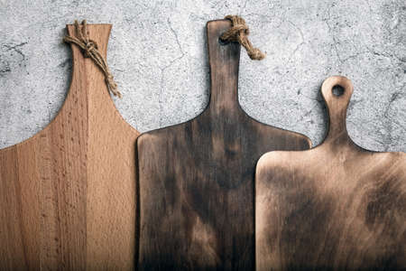 Samples of three different rustic wooden cutting boards on a kitchen countertop against a concrete wall. Manufacture of household goods and accessories made of wood.の写真素材