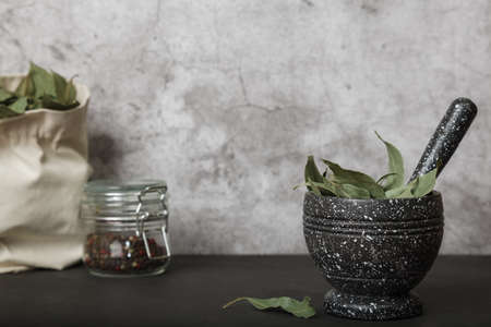 Food background with copy space. Dried bay leaf in a mortar and linen bag, black pepper in a glass...