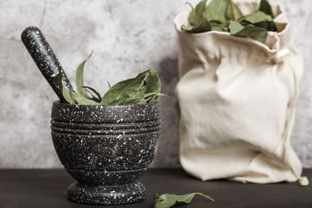 Food background with spices with copy space. Dried bay leaf in a mortar and linen bag on a kitchen countertop.の写真素材