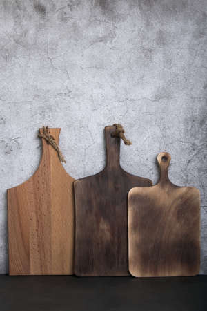 Samples of three different rustic wooden cutting boards on a kitchen countertop against a concrete...