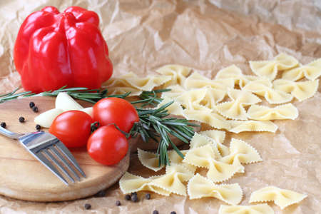 Raw farfalle pasta with cherry tomatoes and red peppers on a light backgroundの写真素材