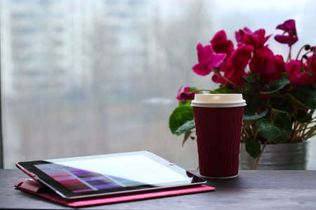 Open tablet PC and cup of coffee. Window of city.の写真素材