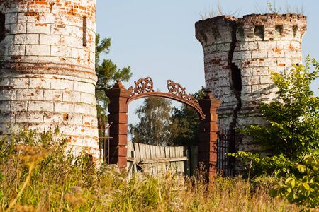 Metal doors with decorative elements and dilapidated towers at the entrance of an old castleの写真素材