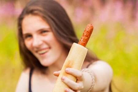 Young smiling girl offering a hot dog for us, focus on it. Summer sunny dayの写真素材