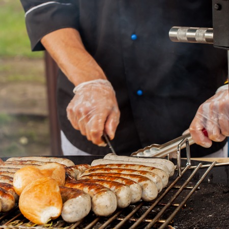 Close-up of a hands man, dressed in a black shirt, cooking spicy browned sausages on the hot grill . Grill conceptの写真素材
