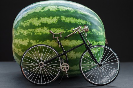 Small model of a retro vintage bicycle near a big whole watermelonの写真素材
