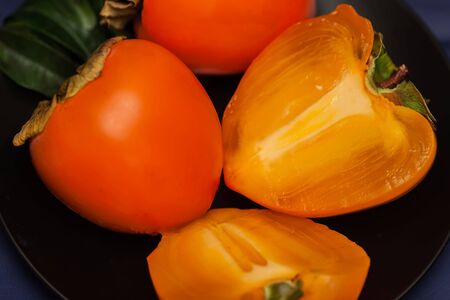 Cut a ripe persimmon in black plate, low key. Sweet, delicious flesh of Persimmon is packed with...