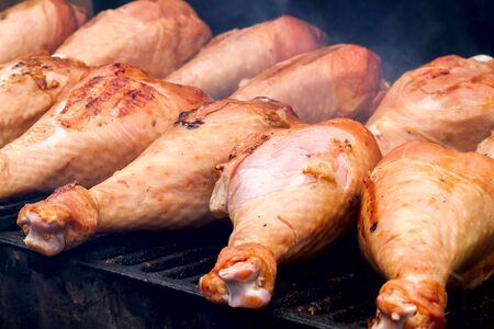 Fresh turkey drumsticks grilling on charcoal stove with fire and smoke, some smokeの写真素材