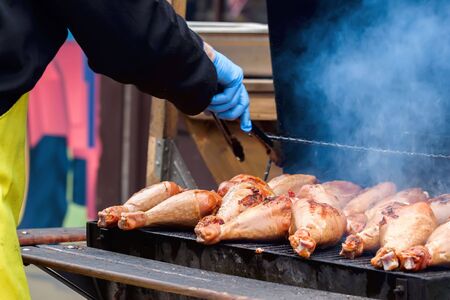 Man's hand with a Grill tongs flips turkey legs fillets on the barbecue to not burnt, with smokeの写真素材