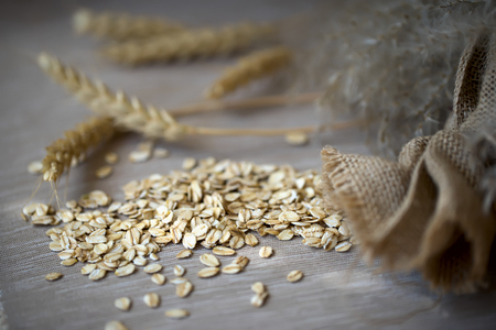 Close-up raw Oat flakes, cereal spikes and sack against a plain coarse linen napkin. Concept of...