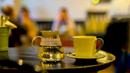 Cup of coffee or tee, glass teapot of hot water, morning. Image with blurred cafe visitors in a low key, for background useの写真素材