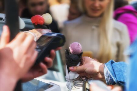Queue for a variety of types of Delicious fresh ice cream with a new taste in black wafer horns. Payment via terminal by credit card. Real sceneの写真素材