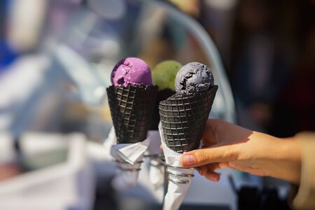 Close-up of three diverse Ice-cream in Black waffle cones. Close-up hand of the girl buyer. Selective focus. Real scene in the store. Copy spaceの写真素材