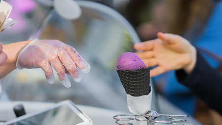 Close-up hands of the buyer and seller. Ice cream stand. Black waffle cone with Ice-cream pink-purple color. Real scene in the store. Copy spaceの写真素材