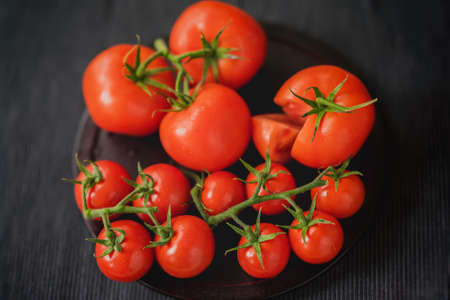 Fresh red ripe tomatoes with water drops on branches on black background. Close-up. Selective focus....
