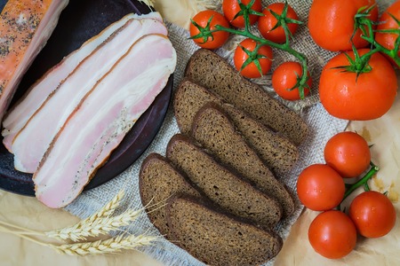 Close-up view of slices of pink bacon, pieces of rye bread, ripe red tomatoes. Fresh organic Food. Quick tasty snack. Top view. For background, that stimulates appetiteの写真素材