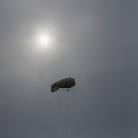 Light coloured blimp, hot air airship in grey sky. Rainy day, unearthly fantastic, but a real landscape. Inflatable dirigible. Abstract square background.の写真素材