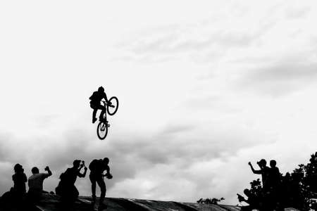 Extreme cyclists, young man doing jump with bmx bike on background of black and white silhouette and cloudsの写真素材