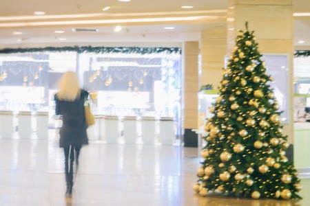 Abstract defocused motion blurred unrecognizable blond girl with long hair in shopping center hurry to buy gifts for loved ones in pre-Christmas holidays, festive backgroundの写真素材