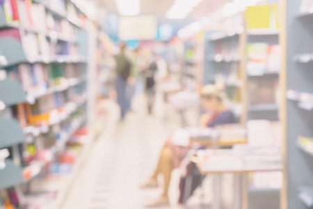 Blurred bookshelves in book store or in library. Unrecognizable silhouettes of people, chooses necessary book. Education concept, reading fiction, life styleの写真素材