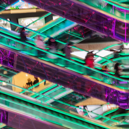 Abstract blurredn image of shopping mall, unrecognizable silhouettes of people on escalators with...
