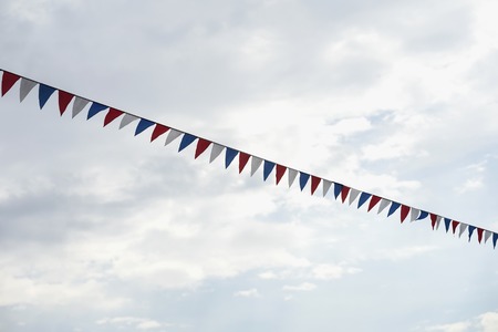 Close-up garland of multi colored flags of triangular shape, pennants in blue sky. Modern background, banner design. Fest, city street holiday, celebration conceptの写真素材