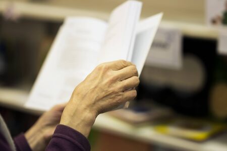 Close-up of hands of the elderly person with open book, bookstore. Real scene. Education concept, Self-study, reading fiction, pension, interests in elderly, life styleの写真素材