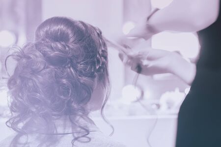 Unrecognizable girl back to us, girl in mirror at hairdresser making hairstyle, styling from long hair, hair salon, partially visible hands master. Blurred, tonedの写真素材