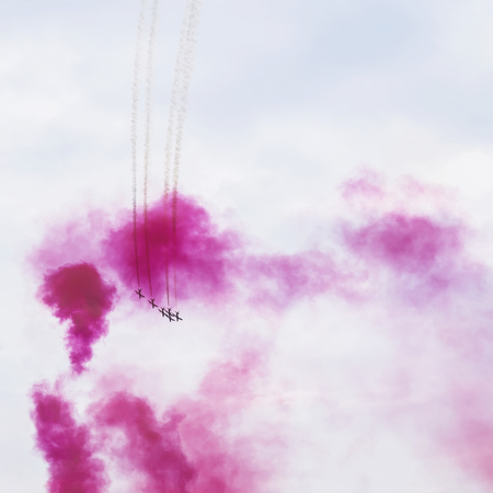Group of aircraft flying in bright, ring of smoke, sangria color.