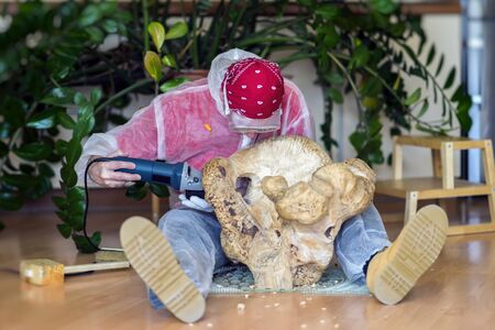 Man woodcarver carving from natural wooden stump, precious wood, art object for decorating house. Concept of handmade, professionalism, hobbyの写真素材