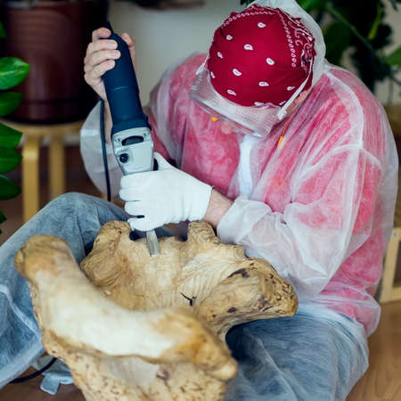 Woodcarver with glasses carving from natural precious wood, art object for decorating house. Hands with tools close-up. Concept of handmade, professionalism and hobbyの写真素材