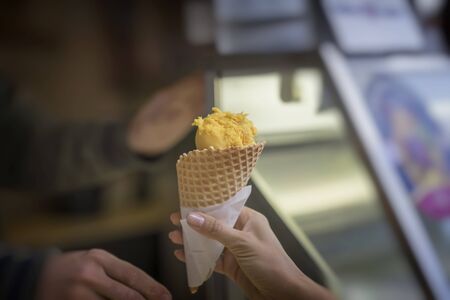 Tasty fruit ice cream is new treat of summer. Cone with yellow ice cream, hit new taste, two hands...