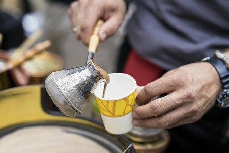 Close-up of hands of man making traditional turkish coffee in copper turk on hot sand and pours freshly prepared into disposable paper cup. Coffee preparation conceptの写真素材