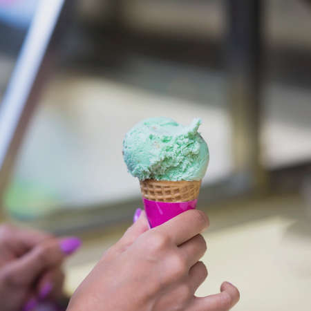 Pistachio ice cream mix in waffle cone, Female hand. Popular delicacies for adults and...