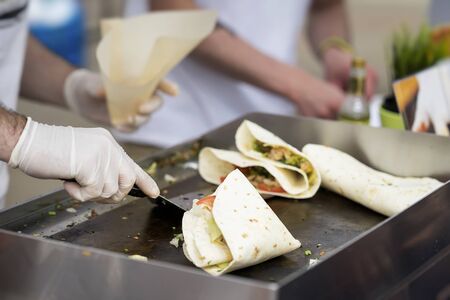 Close-up of hands of cook in latex gloves preparing fajitas or fajitos in park. Healthy fresh tortillas with grilled chicken fillet, avocado, fresh salsa, Mexican foodの写真素材