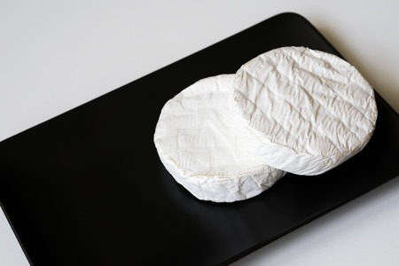 Two heads of camembert or brie cheese in black square plate. Top view. For background, with copy...