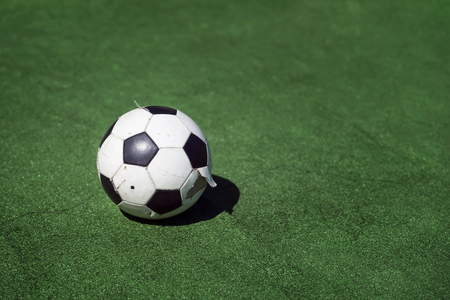 Old, dirty tattered soccer ball on background of green grass. Traditional classic black and white football ball on green field of the stadium training, playground, copy spaceの写真素材