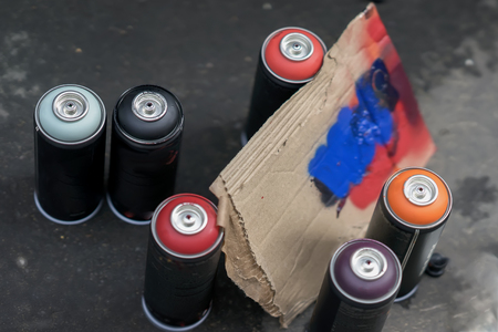 Aerosol cans of spray paint and cardboard palette for paint, graffiti on a dark background of asphalt. Top view. Urban contemporary iconic culture of street youthの写真素材